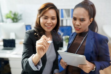 Businesswoman writing equations on glass wall to get amount of sales they should get by the end of the month