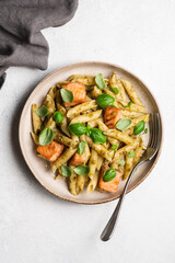 Penne pasta with baked salmon, pesto and fresh basil in a plate, top view, white background