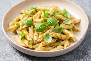Penne pasta with pesto and fresh basil in plate, close up view