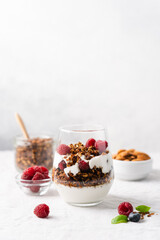 Healthy quick breakfast with yogurt, homemade granola and fresh berries in a transparent glass on table covered with tablecloth and white background. Copy space, close-up view