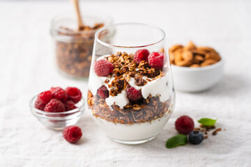 Healthy quick breakfast with yogurt, homemade granola and fresh berries in a transparent glass on table covered with tablecloth and white background. Copy space, close-up view