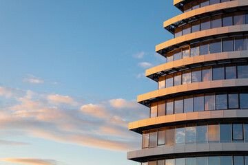 Fragment of modern glass facade of the building under construction against background of sky with clouds. Office or residential building at sunset. Copy space.