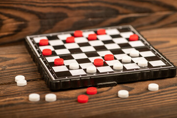 A board for playing checkers with chips on a wooden table, close-up, selective focus.