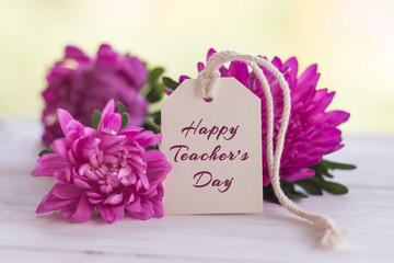 Flowers and tag with the inscription Happy Teacher's Day on a white wooden background. Greeting card concept for teachers day. Close-up