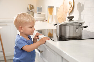 Curious little boy exploring electric stove in kitchen