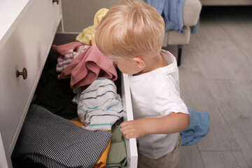 Cute little boy playing with clothes in dresser's drawer at home