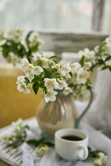 Jasmine flowers in a white vase. Stillife with jasmine and cup of coffee.