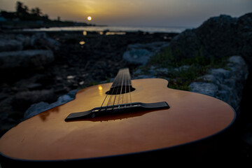 Closeup shot of a brown wooden guitar on the rocks at the seaside during late sunset in Havana, Cuba