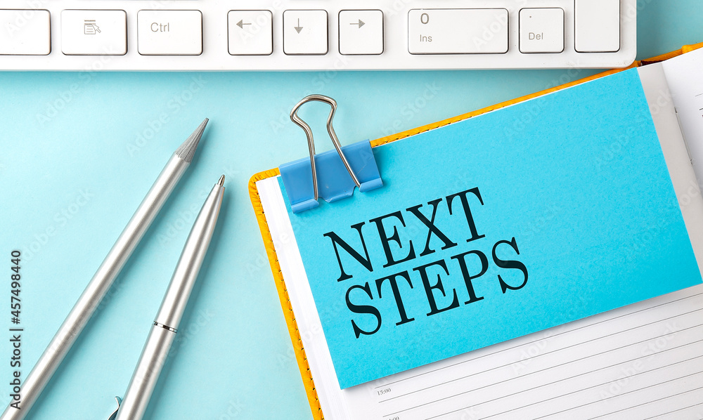 Poster next steps text on sticker on the blue background with pen and keyboard