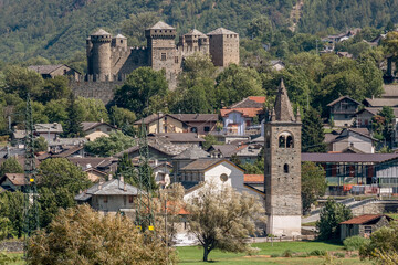 The bell tower of the parish church of San Maurizio, with the imposing castle of Fénis in the background, Aosta Valley, Italy