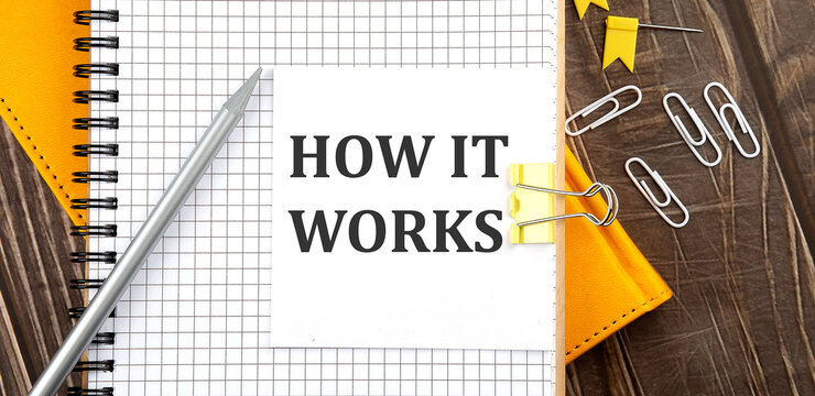 HOW IT WORKS text on a sticker on notebook, wooden background
