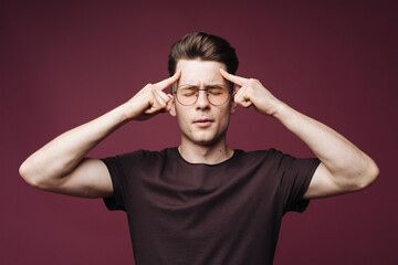 Fototapeta premium Young man in white t-shirt squeezing head with hands, suffering from headache. People, stress, tension and migraine concept