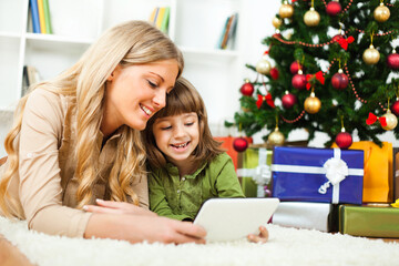 Happy mother and daughter with new year's tree and gift boxes. They are choosing new year's presents online.