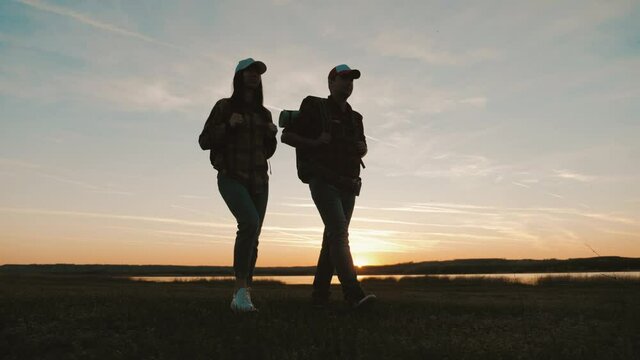 Free travelers concept. Hikers man and woman lovers trekking walking with backpacks in trail. Silhouette hikers walking in the outdoors on the sunset background. Happy couple of travelers.