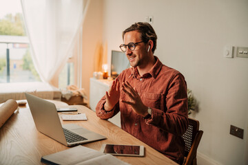 Caucasian male student studying from home listening to lectures with earphones interacting using laptop