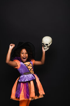 Amazed African American Kid In Witch Halloween Costume Holding Skull Isolated On Black