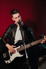 Obraz premium Talented handsome young guitarist man singing a song in studio recording on red background surrounded by instruments. Passion, hobby, singer, electric guitar