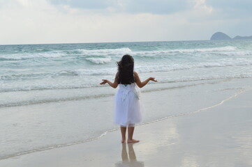 Little girl in white dress, standing on the shore of a crystal clear water beach in Con Dao, Vietnam