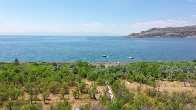 Aerial view Sevan lake, Armenia. Tropical travel. Nice sandy beach with umbrella and beach chair.  Boat in water. Beautiful, touristic place. Trees near lake.