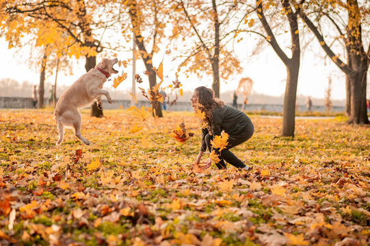 Closeup of curly woman sitting with her dog in autumn leaves outdoors