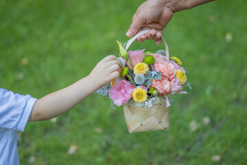 A little kid and his grandma are holding a basket of beautiful, mixed flowers in their hands....