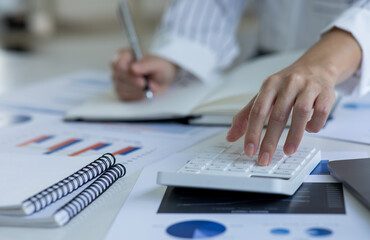 Close up Business woman using calculator and laptop for do math finance on wooden desk, tax, accounting, statistics and analytical research concept.