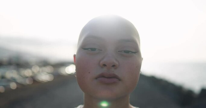Young bald girl looking on camera with sunset in the background