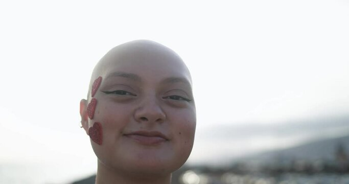 Young bald girl with heart stickers on her face posing in front of camera at sunset