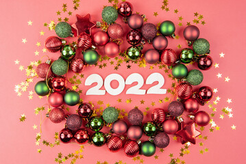 Wooden numbers 2022, green and red toy balls, and stars on a red paper background. Beautiful new year or christmas card top view