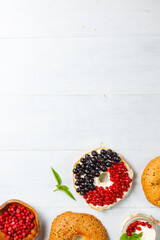 Open bagel with cream cheese, cranberries and blueberries. On a light wooden background. Vertical,...