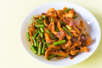 Stir fried crispy pork and yardlong bean with Thai spicy curry paste on white plate in Thai food style.
