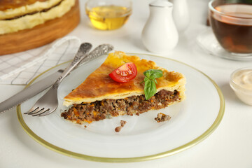 Piece of delicious pie with minced meat, tomato and basil served on white table, closeup