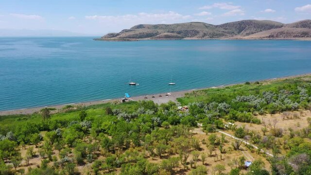 Aerial view peninsula near lake.  Aerial footage Sevan lake, Armenia. Tropical travel. Sandy beach near forest. Trees near lake. Boat in water. Beautiful, touristic place. 