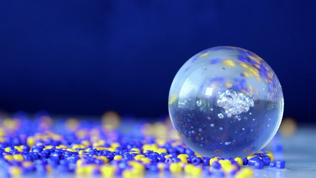 Glass globe on a surface covered by yellow and blue beads. Filmed with sound of bubbling falling water. Closeup