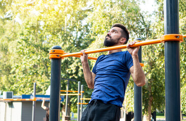 Obraz premium Athletic muscular sportsman trains on the horizontal bar in the city park. Open air training.
