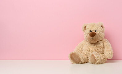 brown teddy bear with a sad face sits on a white table, pink background