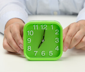 woman's hand holds a green square alarm clock, the clock shows seven in the morning. Wake up early, start the day