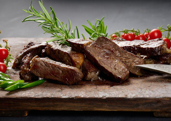 roasted piece of beef ribeye cut into pieces on a vintage brown chopping board, rare doneness
