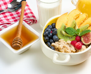 plate with oatmeal and fruit, honey in a bowl on a white table