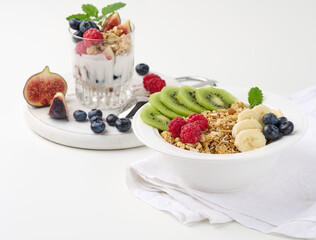 Crunchy in a white round plate with raspberries, kiwi, bananas. Behind a glass with a garnola...