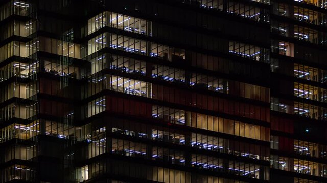Time lapse people working late night, office windows light in business center building facade. Corporate business, high skyscraper glass surface. Lights in building windows turn on and off