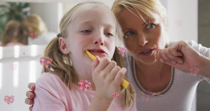 Animation of flower hearts over caucasian mother and daughter brushing teeth