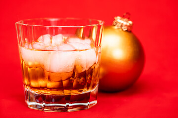 Glass of whiskey with christmas bauble on red background christmas drink concept