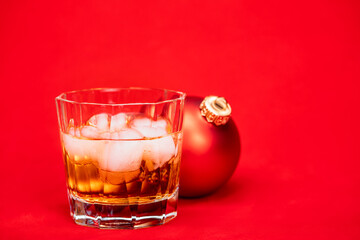 Glass of whiskey with christmas bauble on red background christmas drink concept