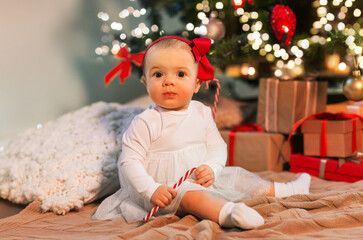 holidays and childhood concept - sweet baby girl with gifts at home over christmas tree lights