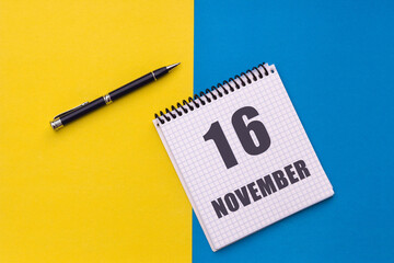 November 16th. Day 16 of month. Calendar date. Notebook with a spiral and pen lies on a yellow-blue background