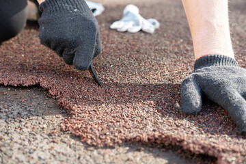 Male hands in gloves are repairing the sports ground, cutting out the damaged area of the special coating with a knife. 