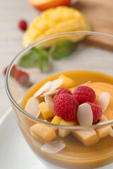 Delicious panna cotta with mango coulis, fresh fruit pieces and almond flakes in bowl, closeup