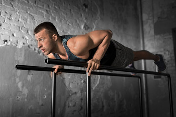 fitness, sport, bodybuilding and people concept - young man doing push-ups on parallel bars in gym