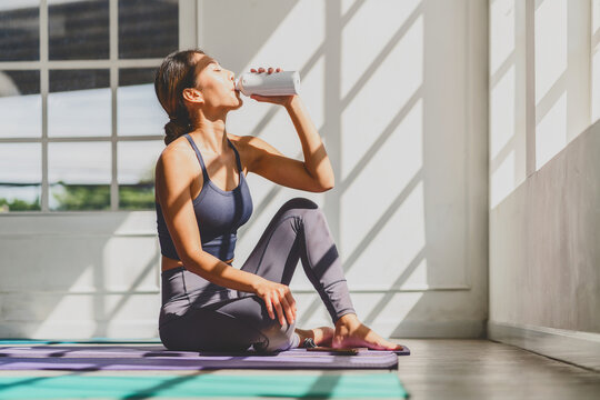 Asian woman drinking after practicing yoga at home on the yoga mats,Exercises at home concept - Powered by Adobe
